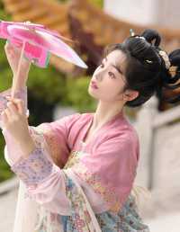 粉伞轻遮笑靥，清风拂面花枝乱